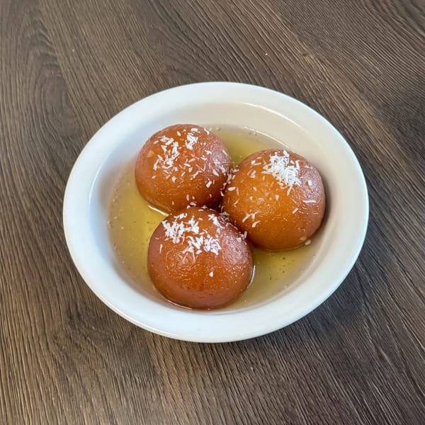 Three gulab jamun, Indian fried dough balls in syrup, topped with coconut flakes on a white plate.