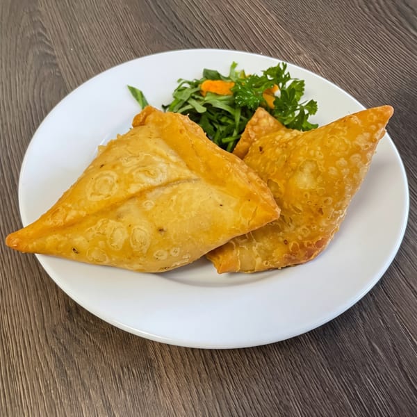 Two golden-brown samosas with a side of fresh green salad on a white plate.