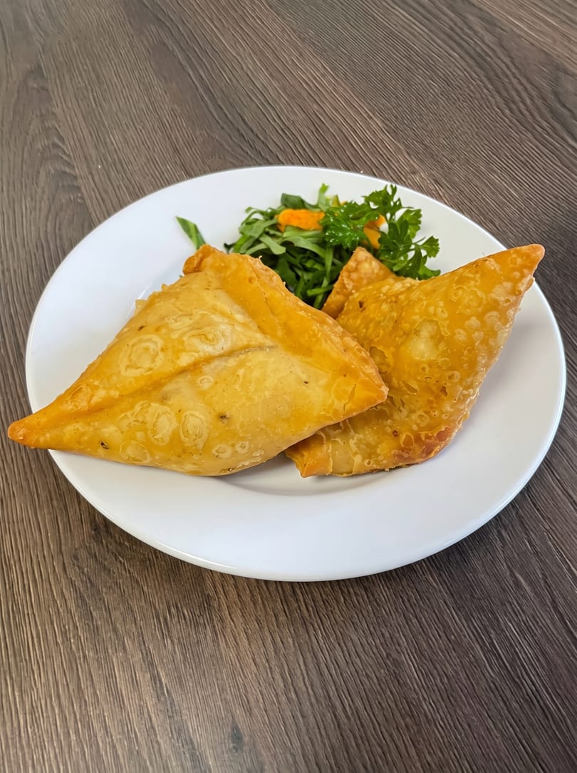 Two golden-brown samosas with a side of fresh green salad on a white plate.